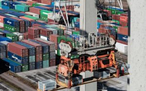 Shipping containers pictured in a yard with a container crane in the foreground.